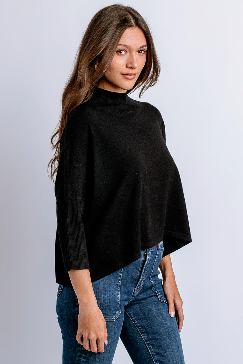 Woman wearing a black mock neck sweater and blue jeans against a light gray background