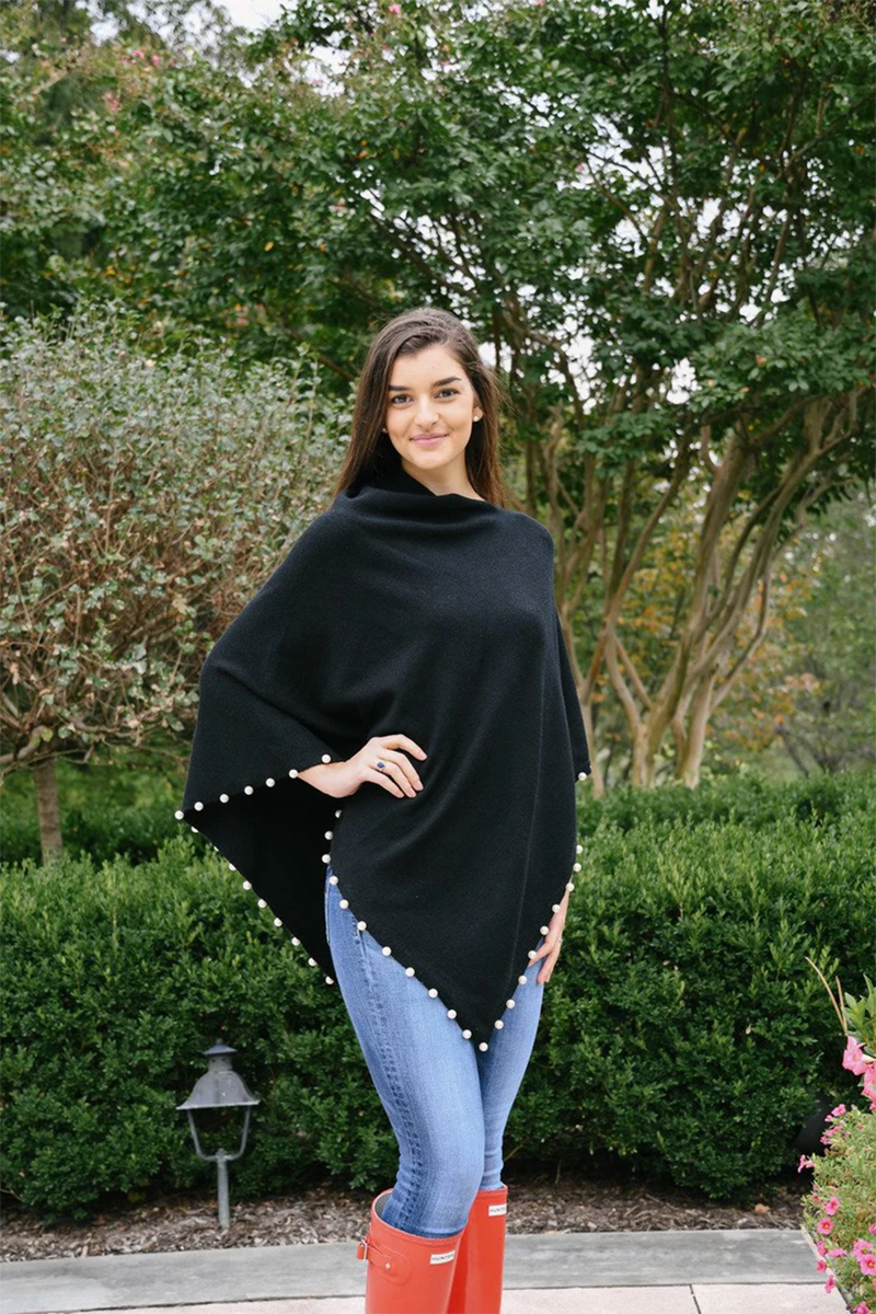 Woman wearing a black poncho with pearl trim, blue jeans, and red boots standing outdoors.