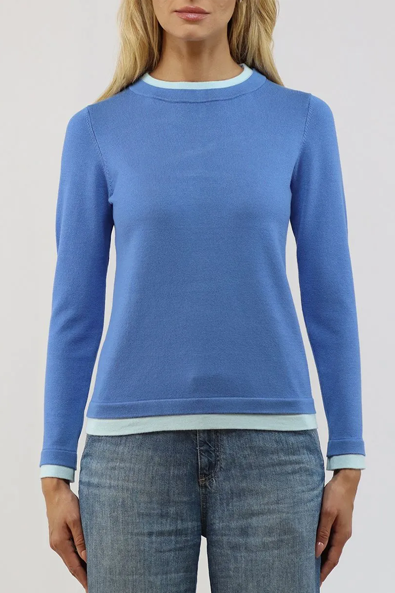Person wearing a periwinkle blue sweater with light blue trim on a plain background