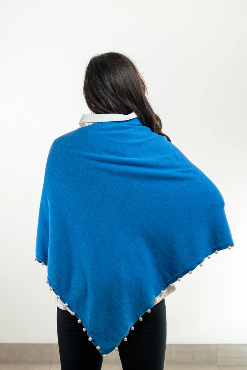 Person wearing a blue poncho with pearl trim on a plain background