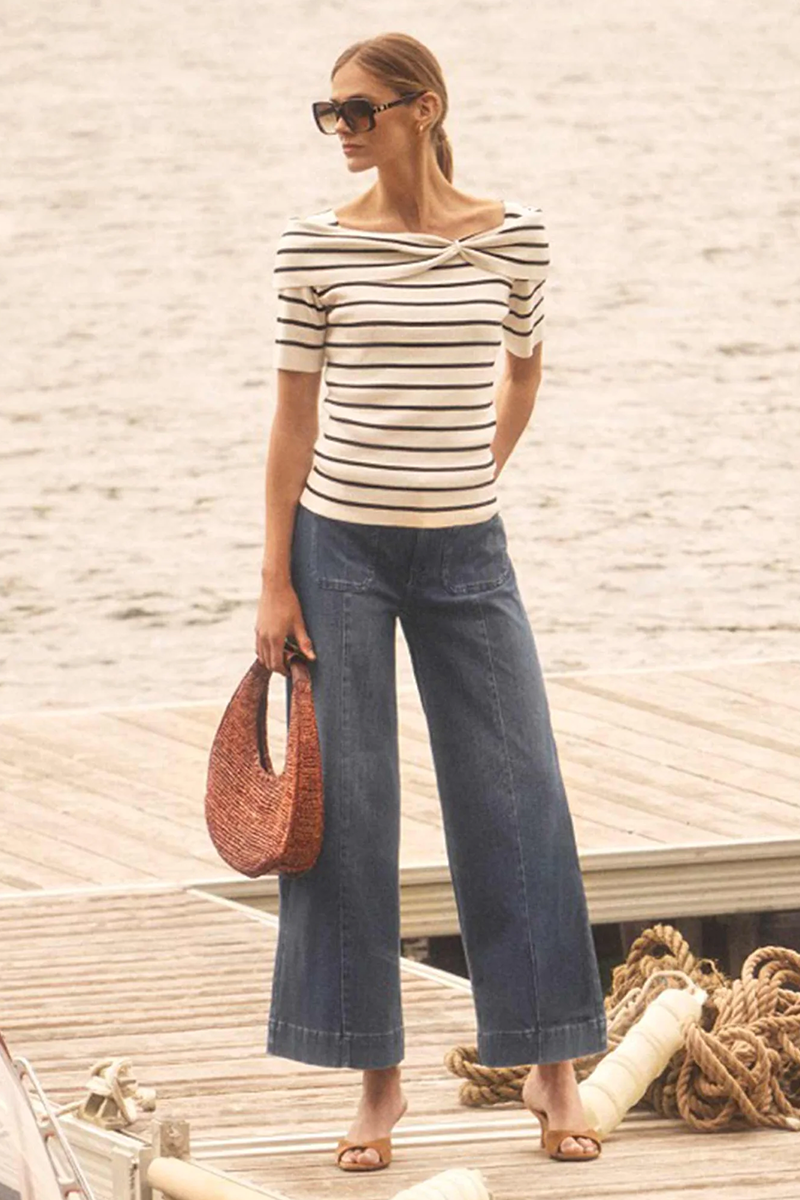Woman in striped shirt and wide-leg jeans standing on a dock with a wooden background