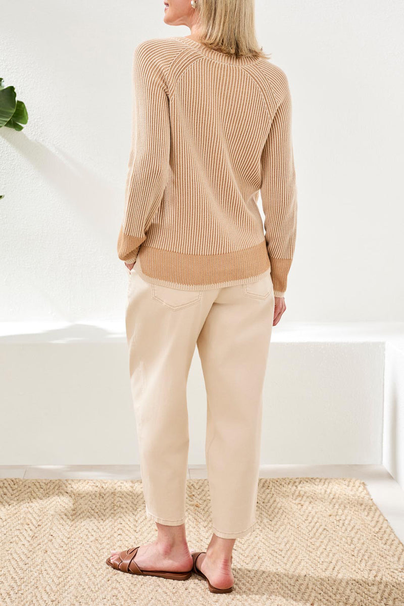 Woman wearing a beige sweater and pants in a minimal indoor setting