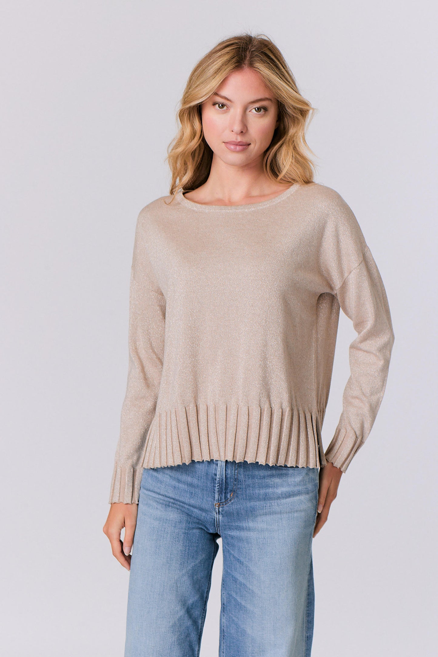 Woman wearing a beige sweater and blue jeans on a light gray background