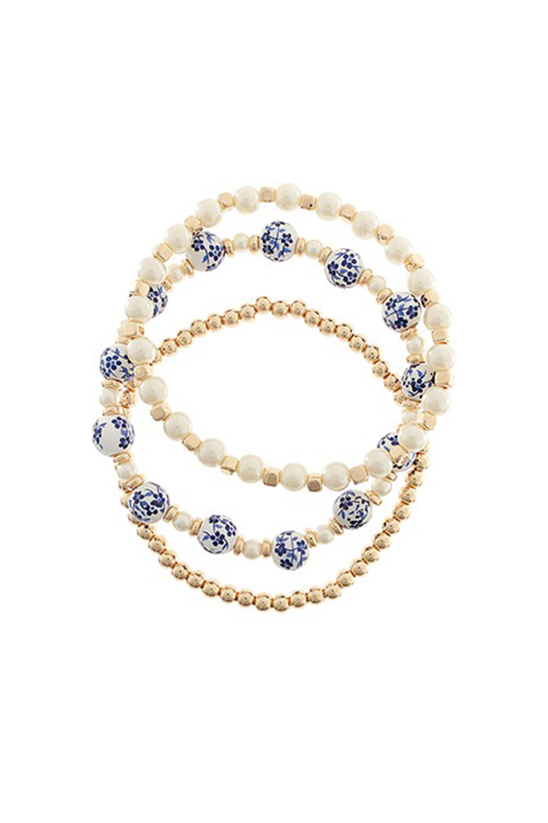 Three layered beaded bracelets with white, blue, and gold beads on a white background