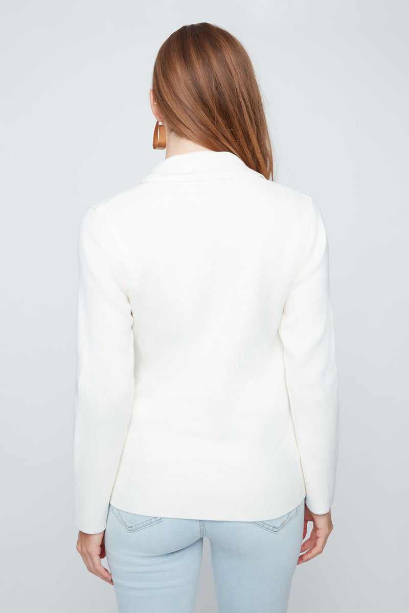 Woman wearing a white blazer and light blue jeans on a plain background