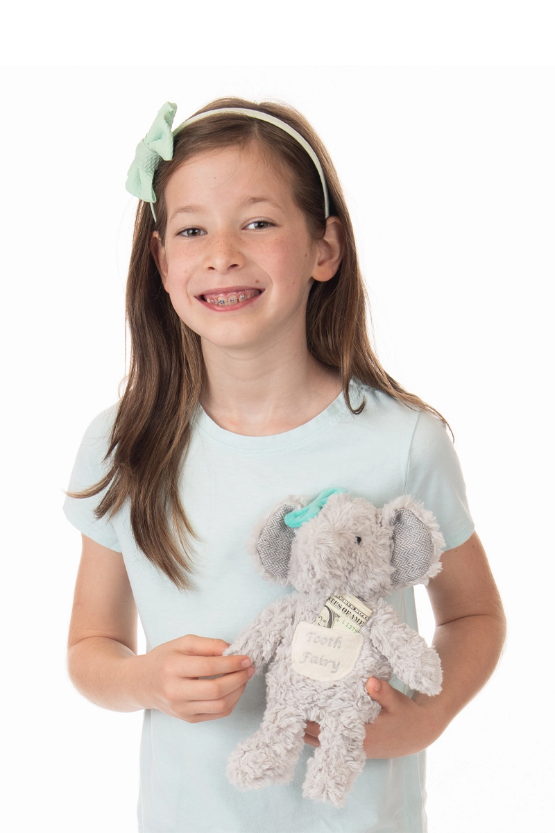 Young girl holding a plush elephant toy with a bow on a white background