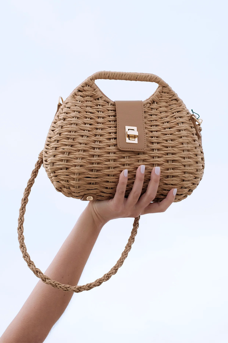 Woven straw handbag held by a hand against a grey background