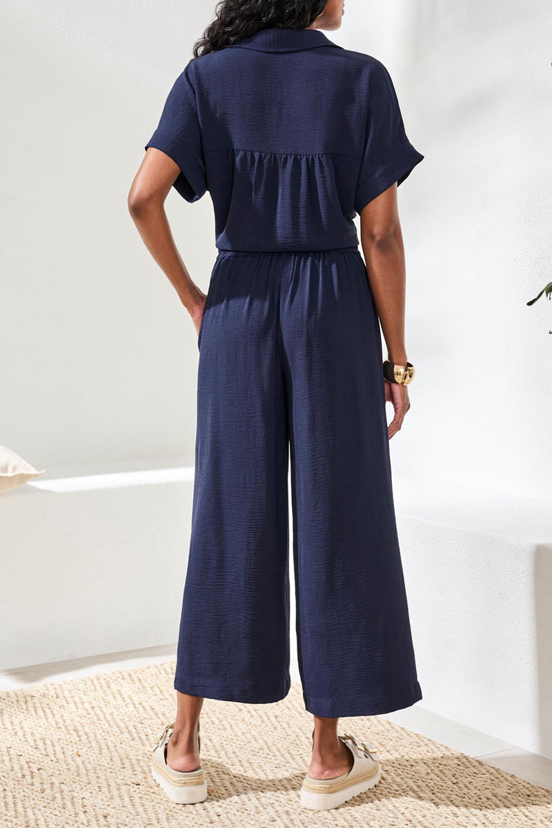 Person wearing a navy blue top and pants standing on a light-colored floor with a white wall background