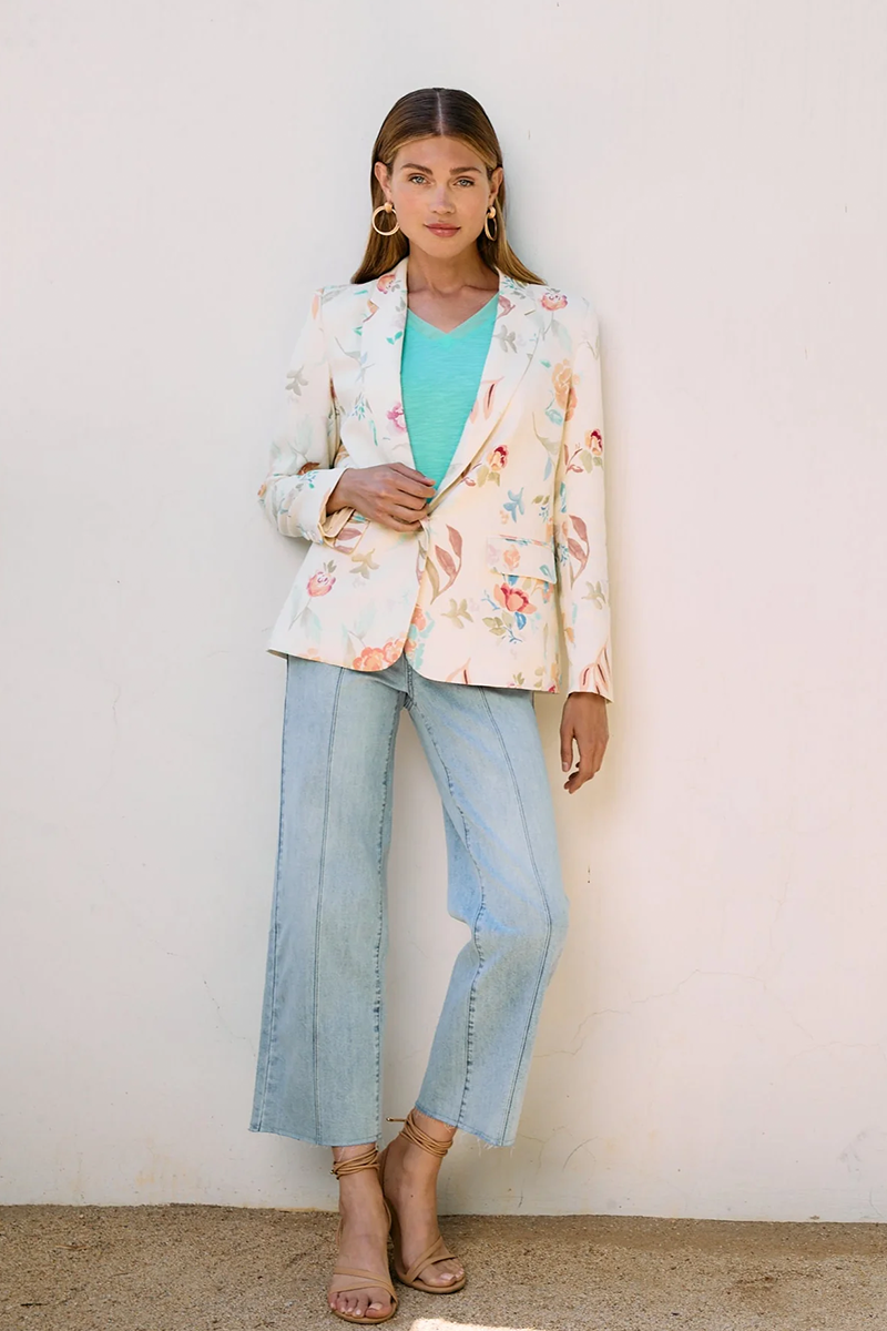 Woman wearing a floral blazer, turquoise top, and light blue jeans against a white background