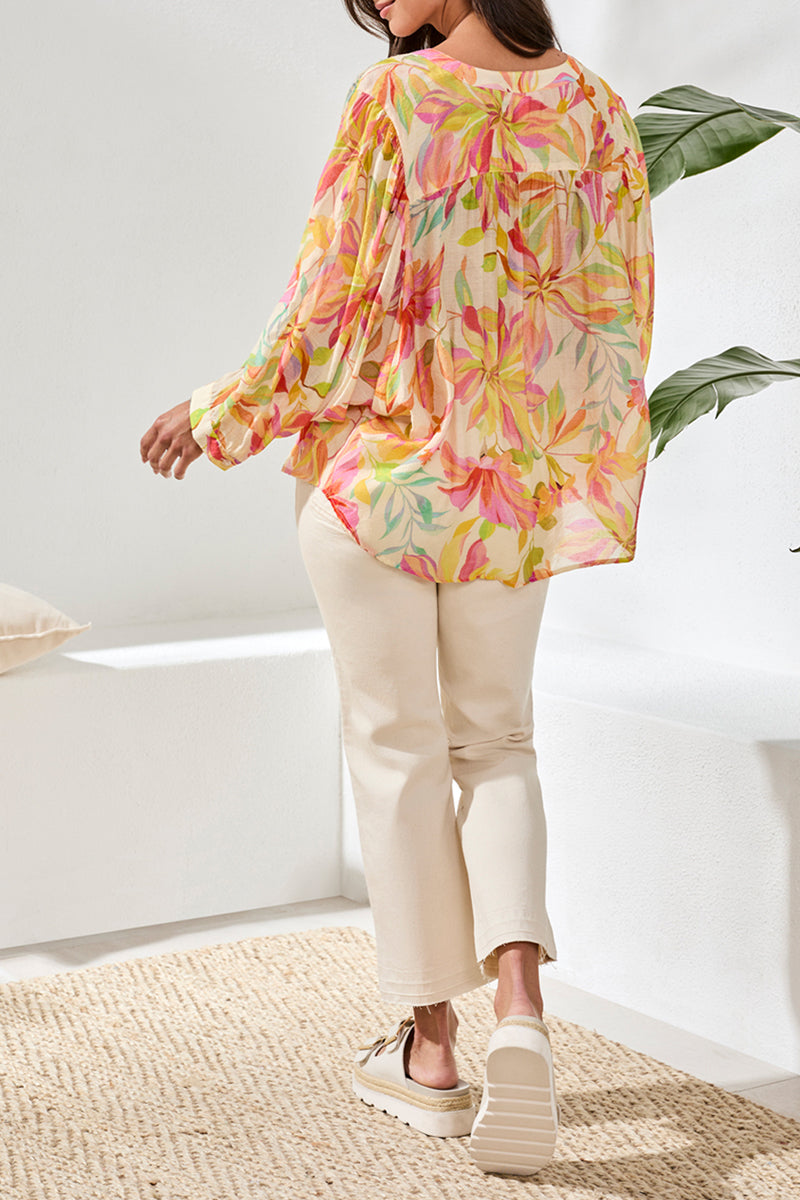 Woman wearing a colorful floral blouse and beige pants in a bright room.