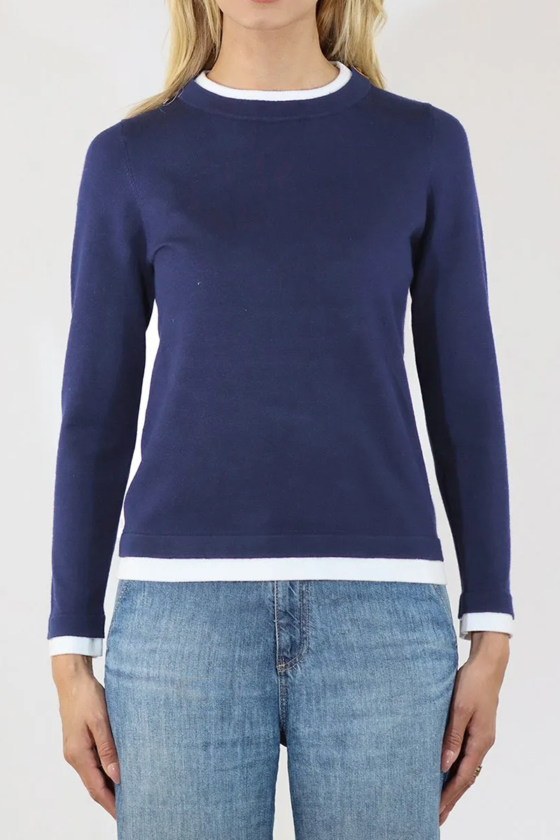 Person wearing a navy sweater with white trim and blue jeans on a white background
