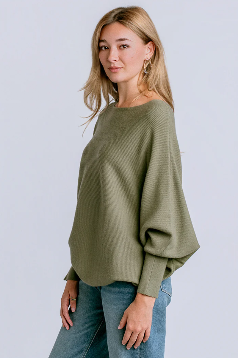 Woman wearing an olive green sweater and blue jeans against a light gray background
