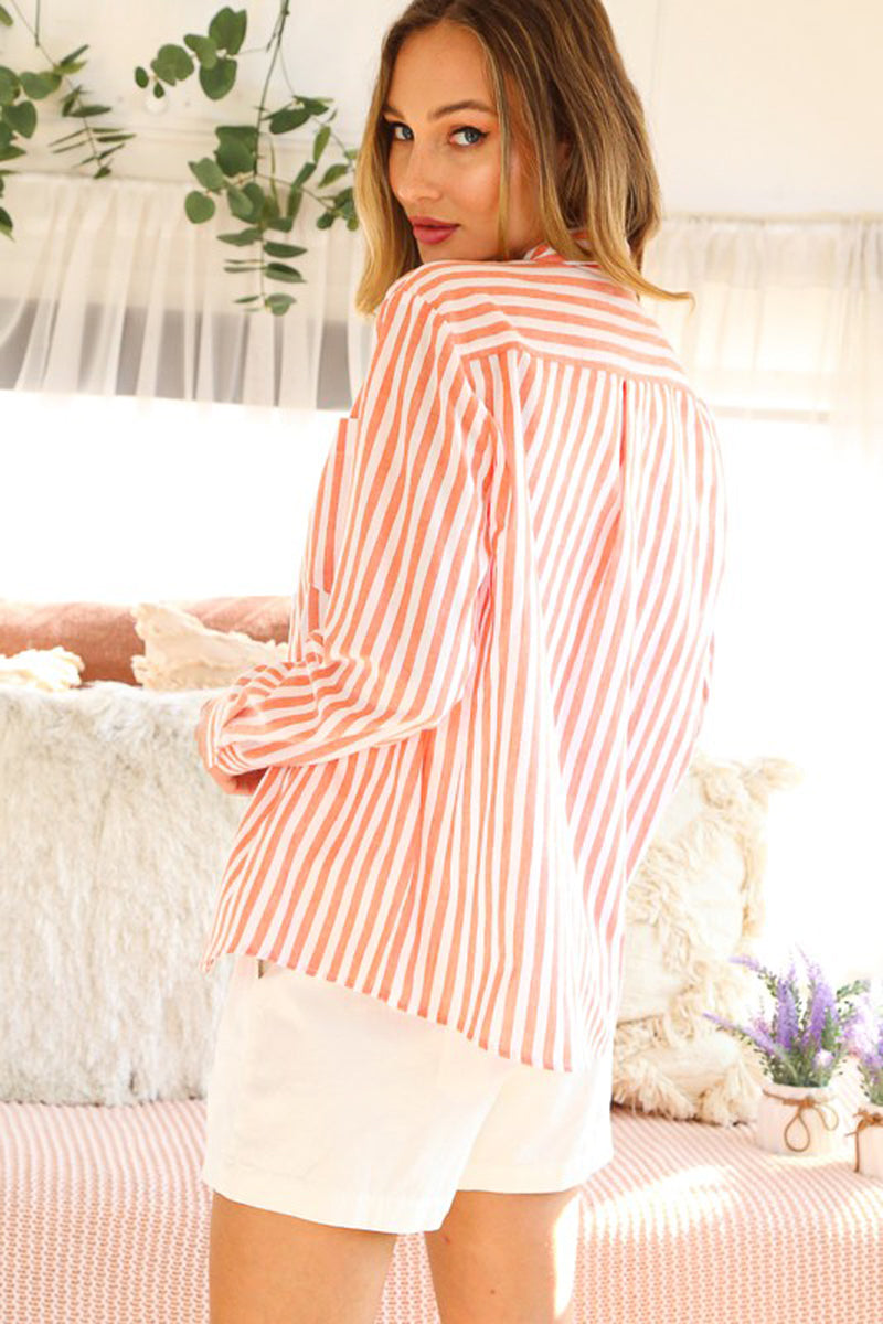 Woman wearing a orange striped shirt and shorts in a bedroom setting