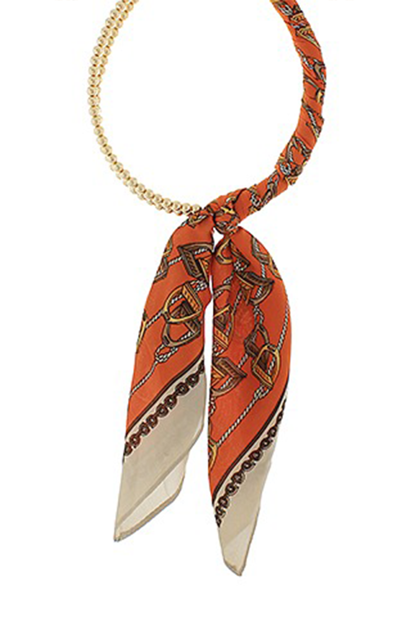 Gold necklace wrapped with an orange and beige patterned scarf on a white background