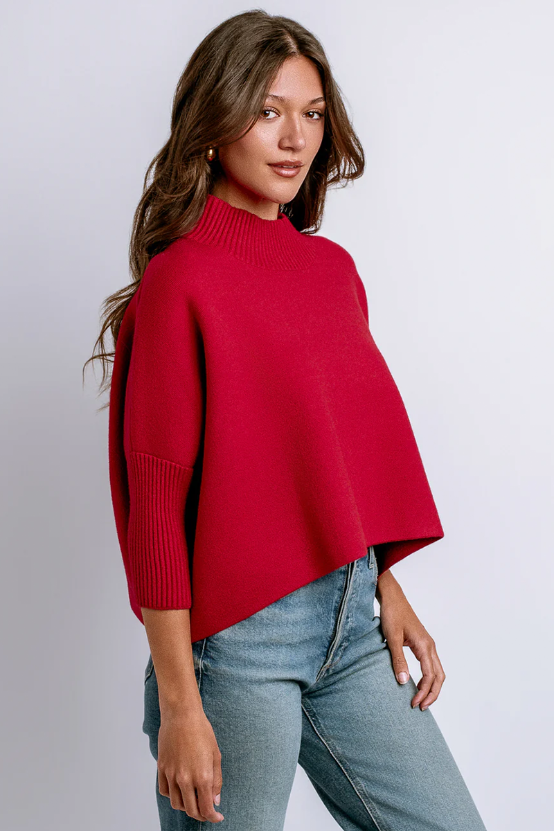 Woman wearing a red mock neck sweater and blue jeans on a white background