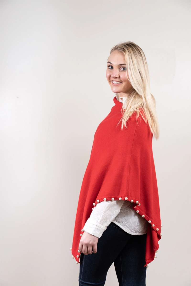 Woman wearing a red poncho with pearl trim on a plain background