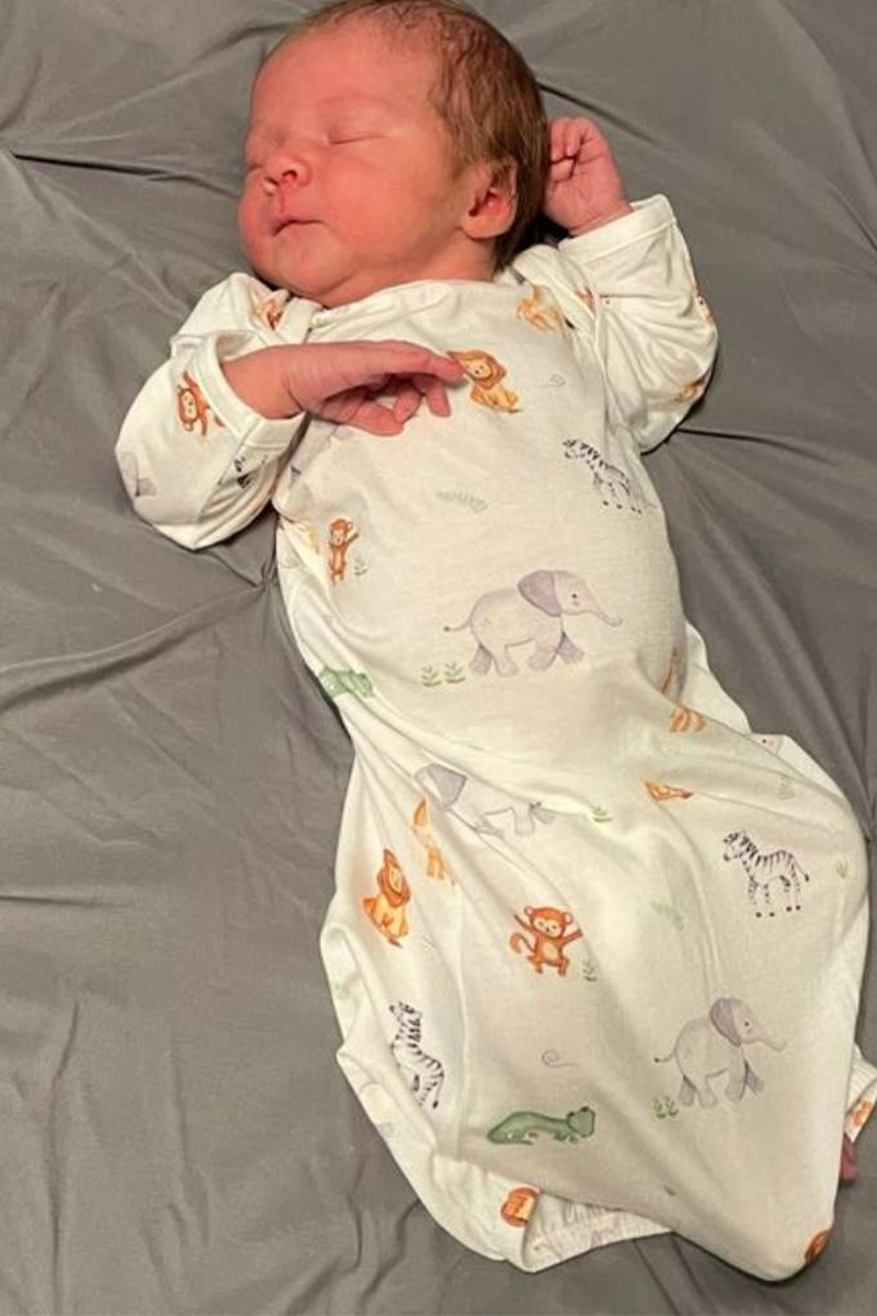 Newborn in an animal blanket sack gown on a gray sheet