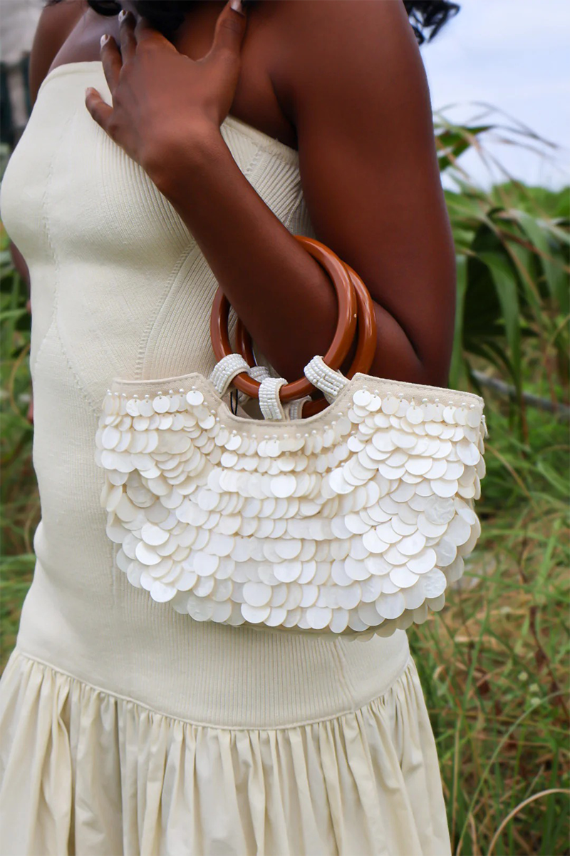 Woman holding a white shell sequined handbag in a natural setting