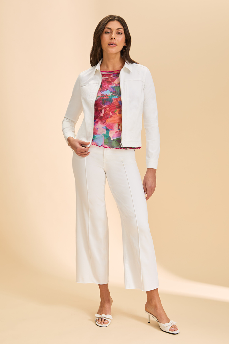 Woman wearing a white jacket, colorful top, and white pants on a beige background