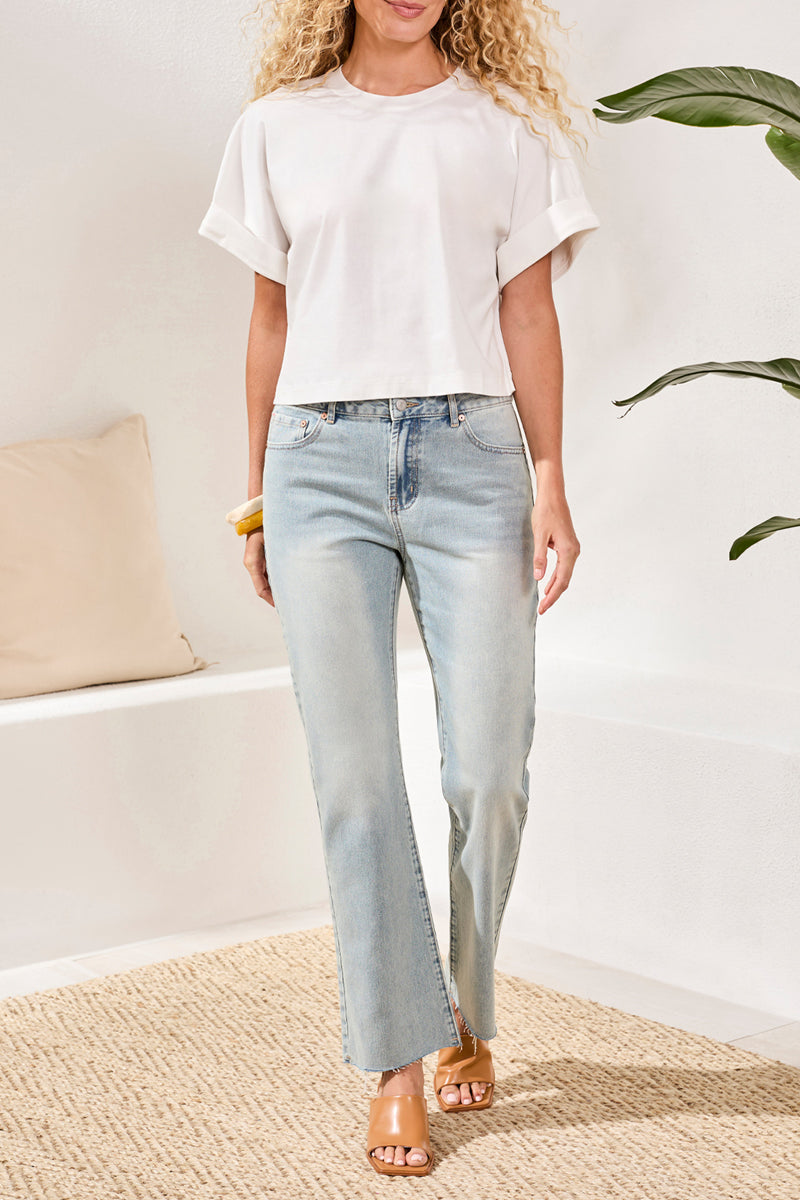 Woman wearing a white top and light blue jeans in a minimalistic room.