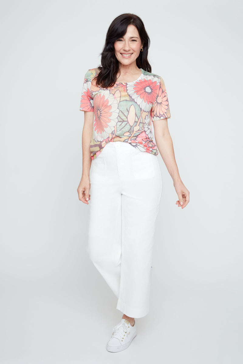 Woman wearing a colorful floral top and white pants on a white background