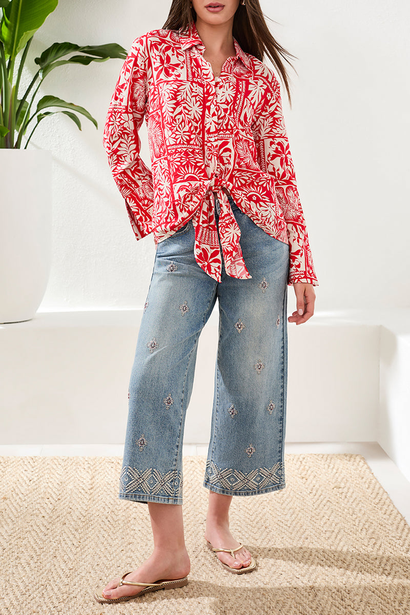 Person wearing a red floral blouse and blue jeans with embroidery indoors.