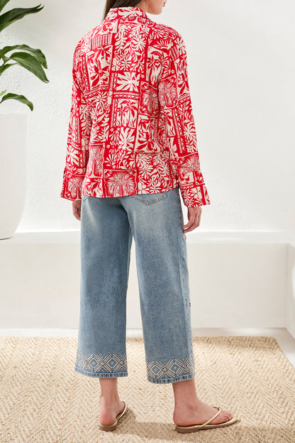 Person wearing a red and white patterned blouse with blue jeans indoors.