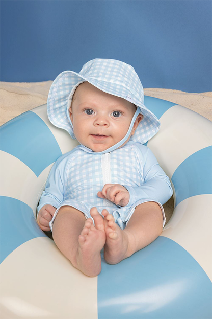 Baby wearing a light blue checkered sun hat and matching outfit on a striped cushion.