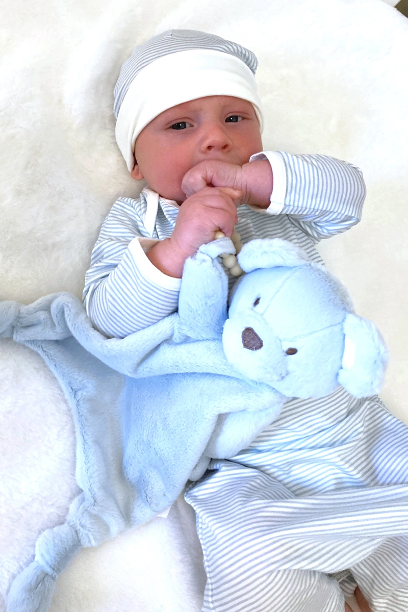 Newborn baby in a striped outfit holding a blue teddy bear on a white background