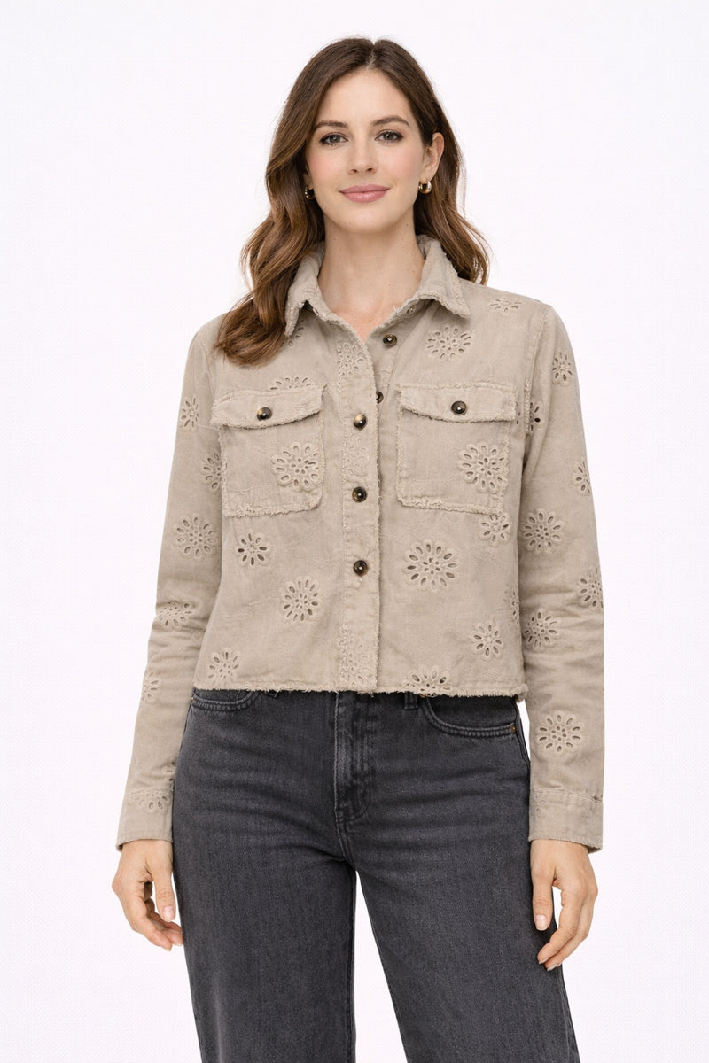 Woman wearing a beige eyelet jacket and dark jeans on a white background