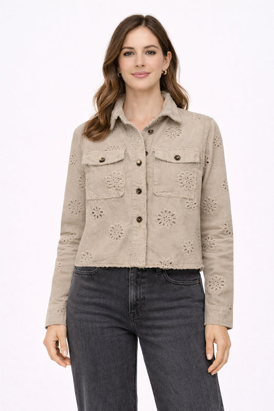 Woman wearing a beige eyelet jacket and dark jeans on a white background