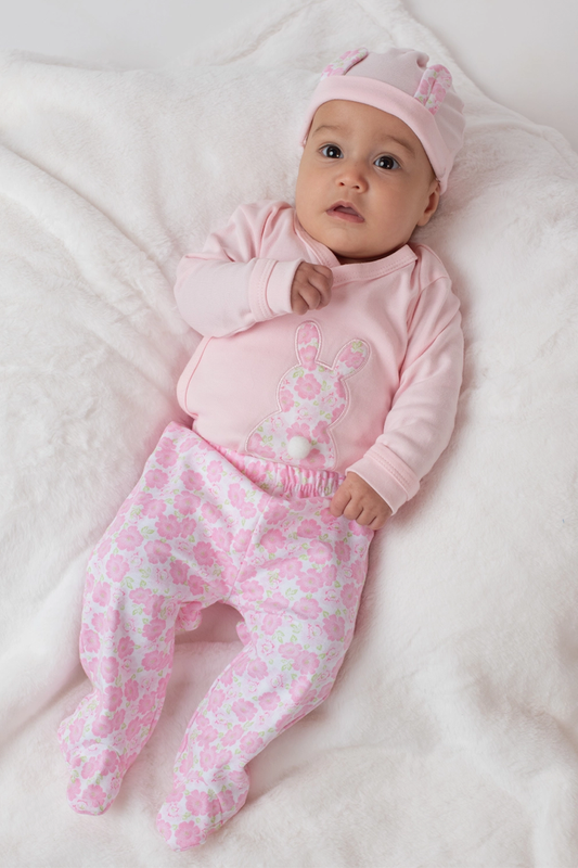 Baby in pink outfit with floral patterns on a white blanket
