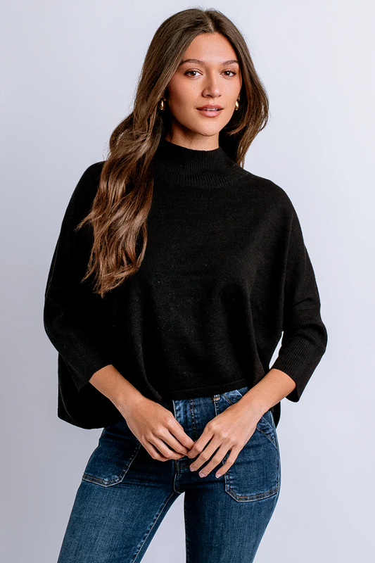 Woman wearing a black mock neck sweater and blue jeans against a gray background