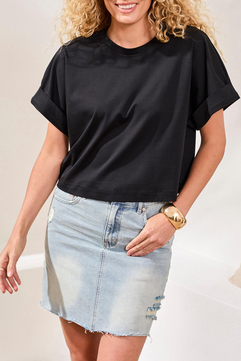 Woman wearing a black oversized t-shirt and denim skirt on a plain background