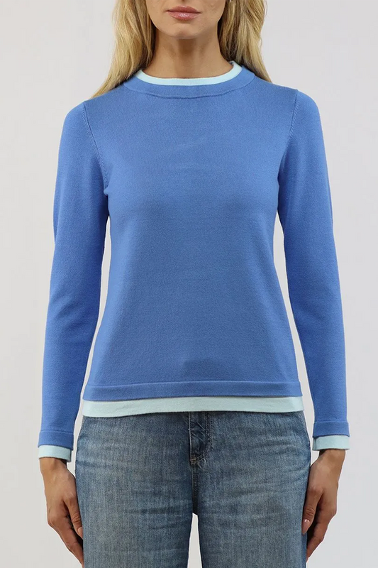 Person wearing a periwinkle blue sweater with light blue trim on a plain background