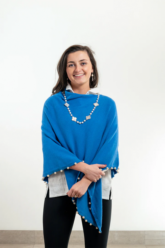 Woman wearing a blue poncho with pearl trim in front of a white background