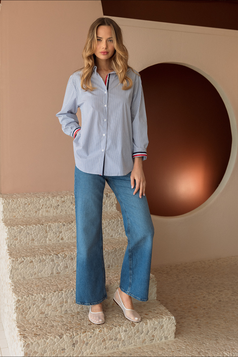 Woman wearing a light blue shirt and jeans standing in a modern indoor setting.