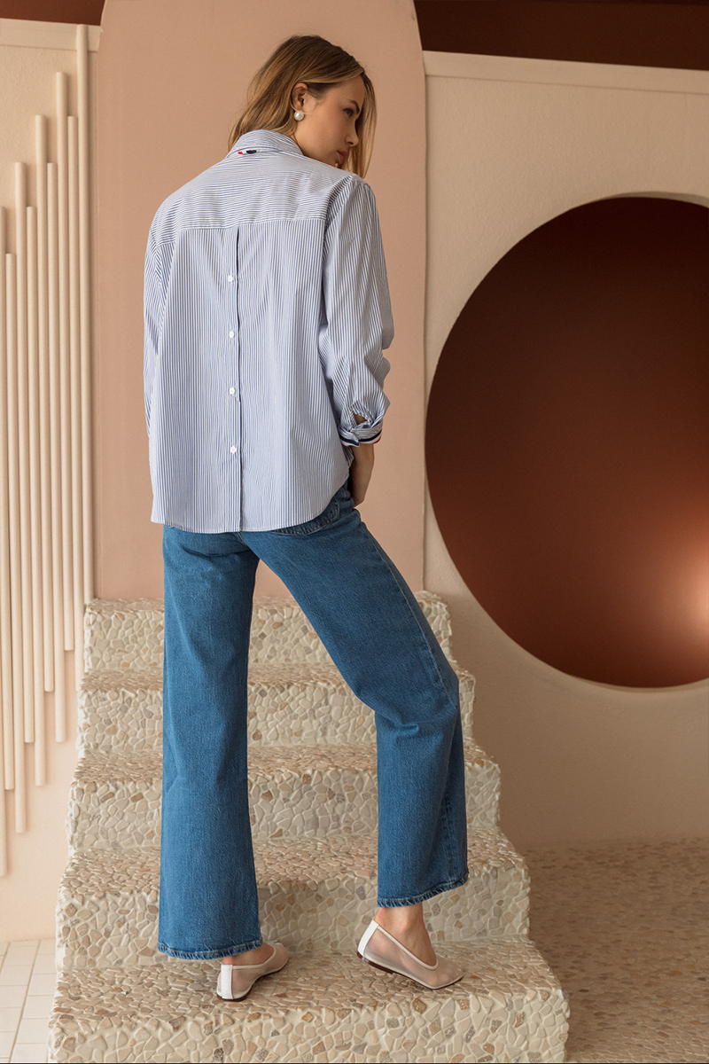 Woman in light blue shirt and jeans standing on a staircase with a decorative wall in the background