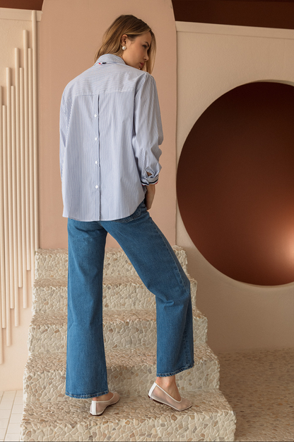 Woman in light blue shirt and jeans standing on a staircase with a decorative wall in the background