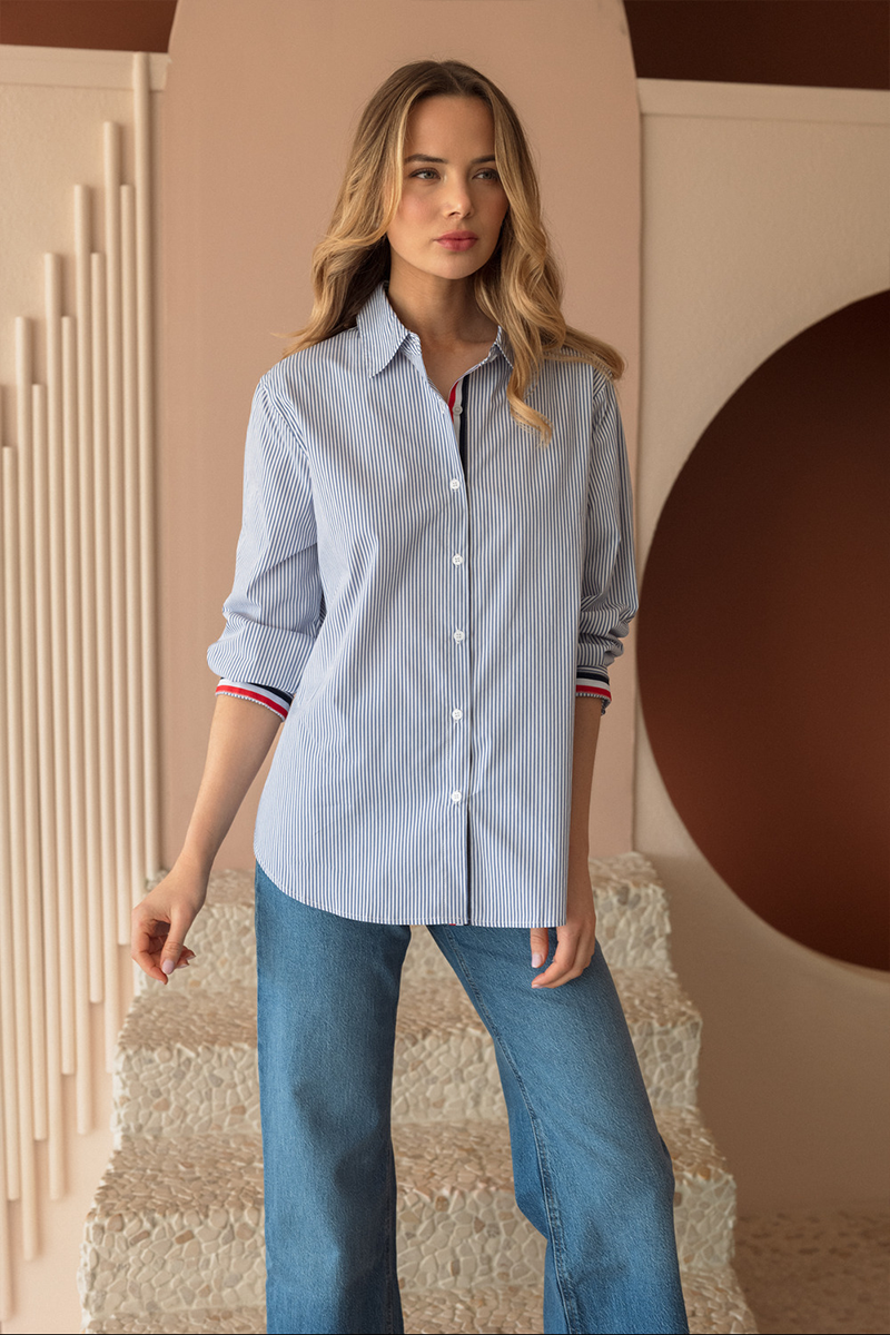 Woman wearing a blue striped shirt and jeans standing against a decorative wall.