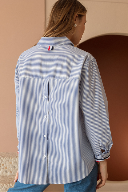 Woman wearing a blue and white striped shirt with a brand logo on a beige wall.