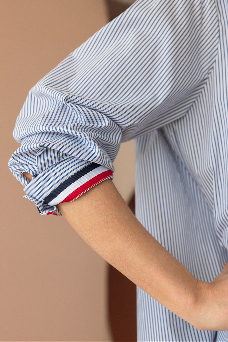 Close-up of a person wearing a blue and white striped shirt with rolled-up sleeves on a beige background