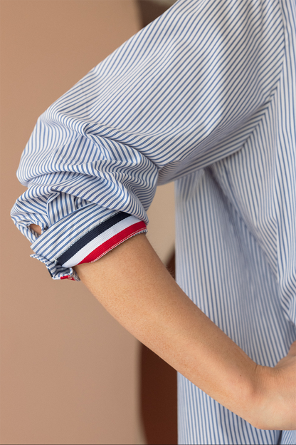 Close-up of a person wearing a blue and white striped shirt with rolled-up sleeves on a beige background