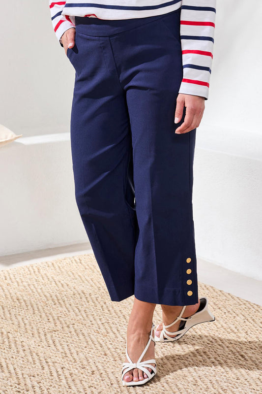 Person wearing navy pants with gold buttons and a striped shirt on a neutral background