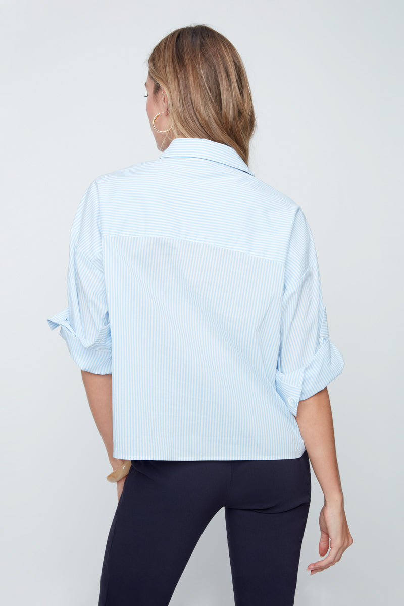 Woman wearing a light blue button-up shirt and dark pants on a plain background