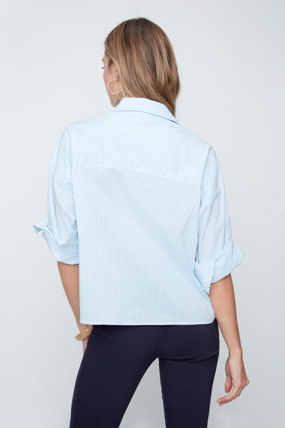 Woman wearing a light blue button-up shirt and dark pants on a plain background