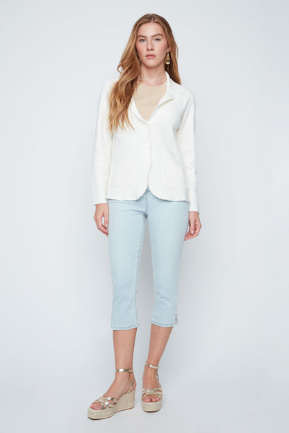 Woman wearing a white blazer, light blue jeans, and sandals on a plain background