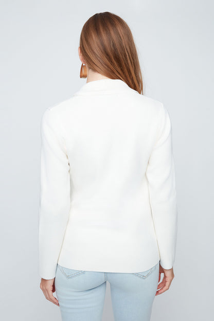 Woman wearing a white blazer and light blue jeans on a plain background