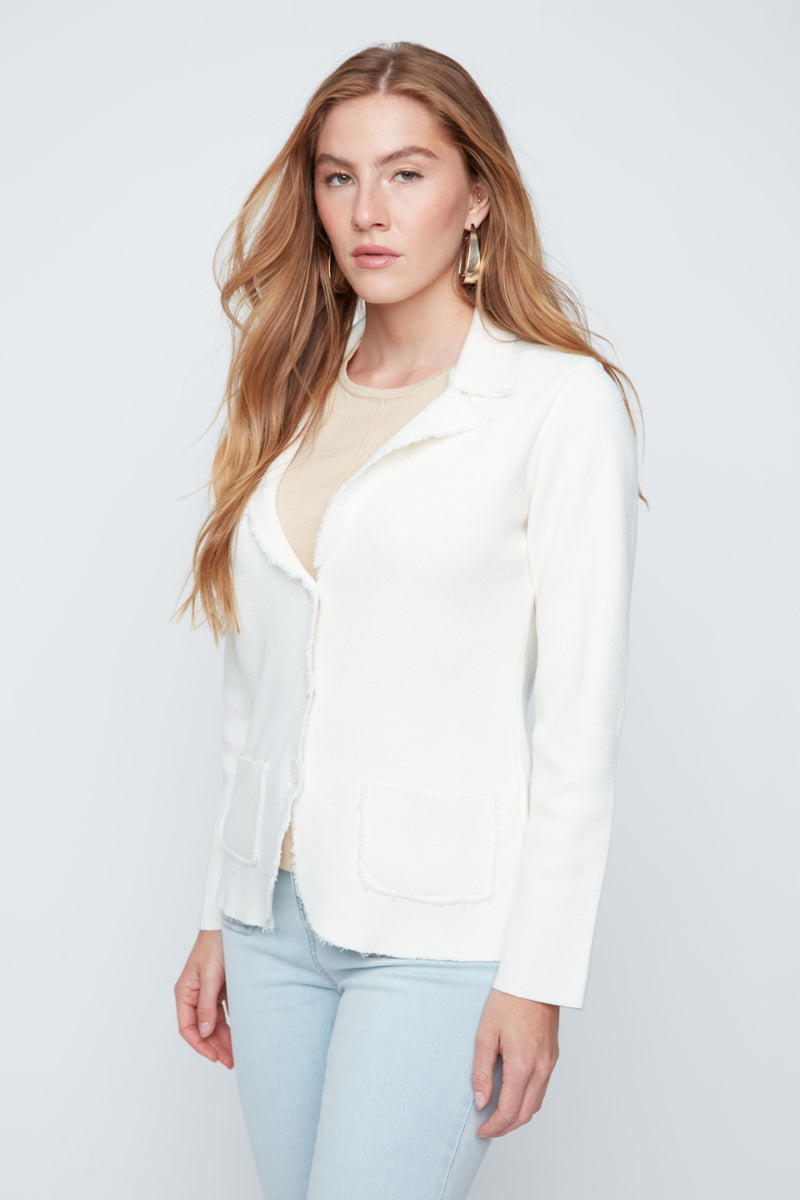 Woman wearing a white blazer over a light yellow top and light blue jeans on a plain background