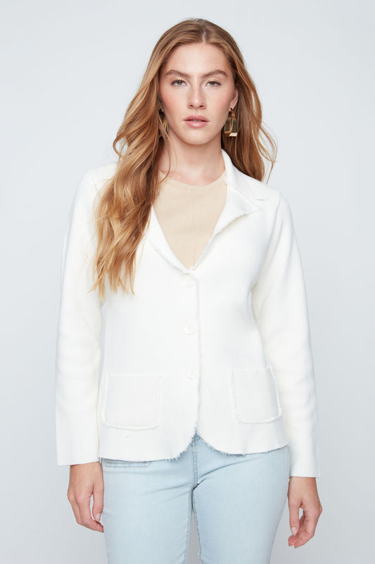 Woman wearing a white blazer over a beige top with light blue jeans on a plain background